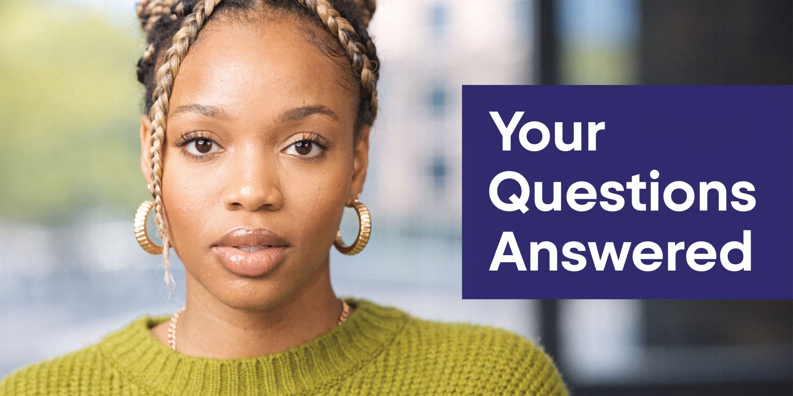A professional portrait of a woman with braided hair wearing a green sweater and gold earrings.