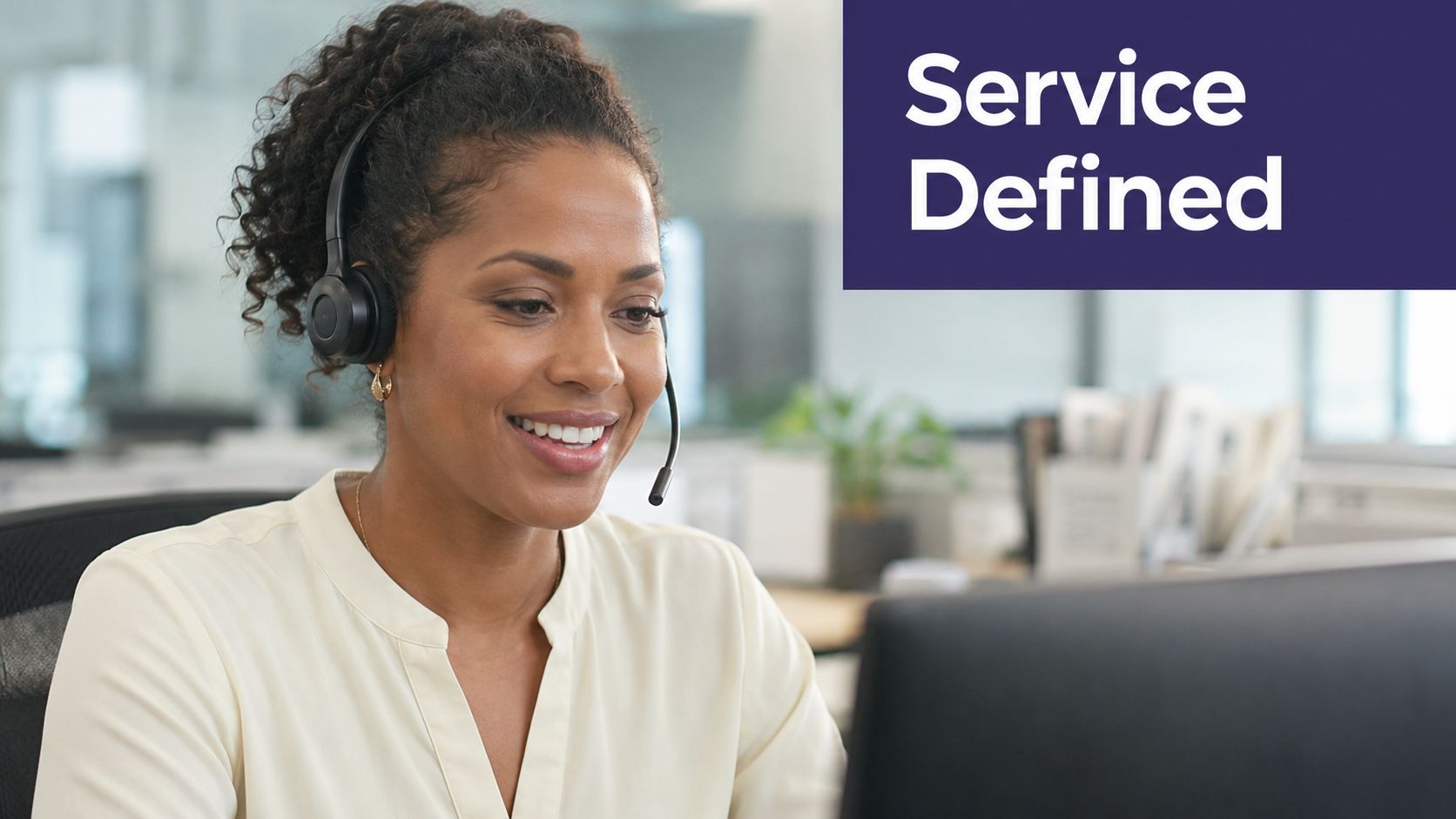 A professional woman wearing a headset, smiling while looking at a computer screen in an office.